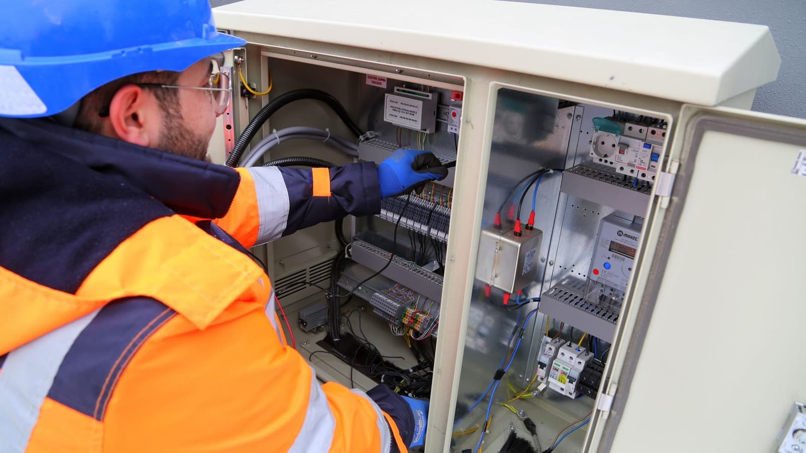 Servicemonteur met helm en handschoenen werkt in een elektrische besturingskast