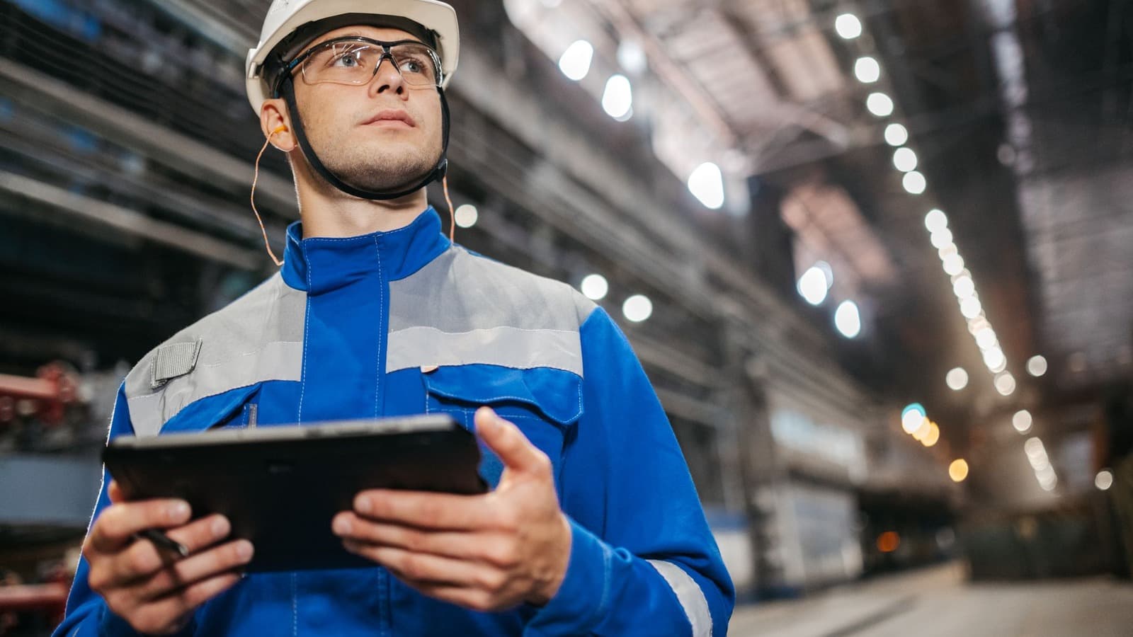 Technisch medewerker met helm, veiligheidsbril en tablet in een fabriekshal