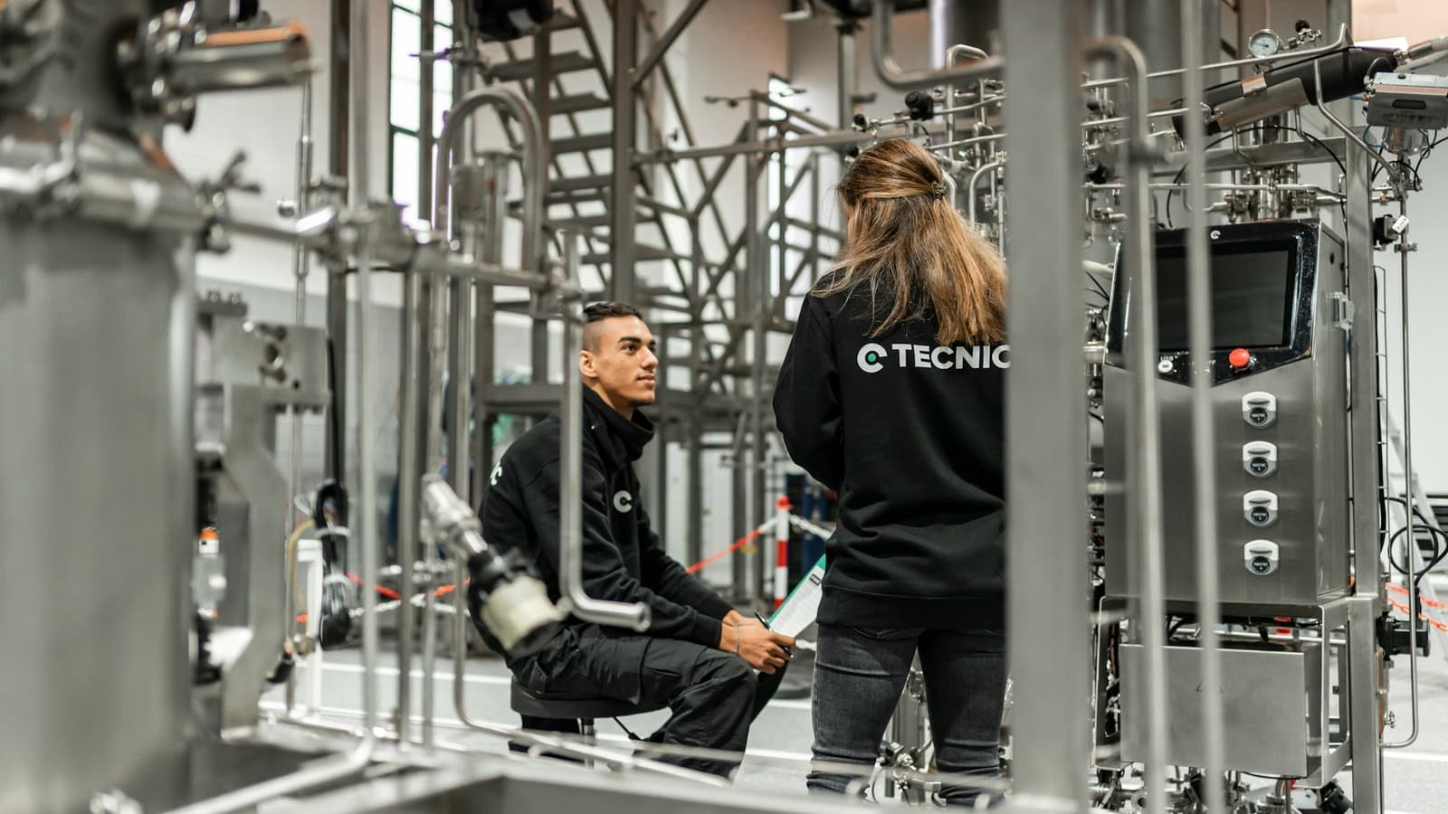 Twee technische medewerkers overleggen tussen industriële leidingen en machines