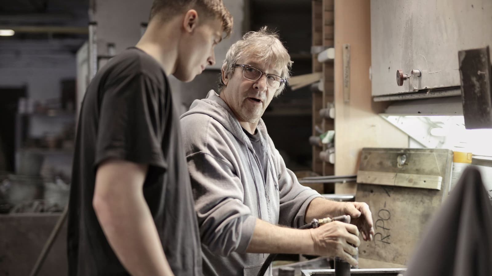 Ervaren vakman geeft een jongere collega uitleg over gereedschap in de werkplaats