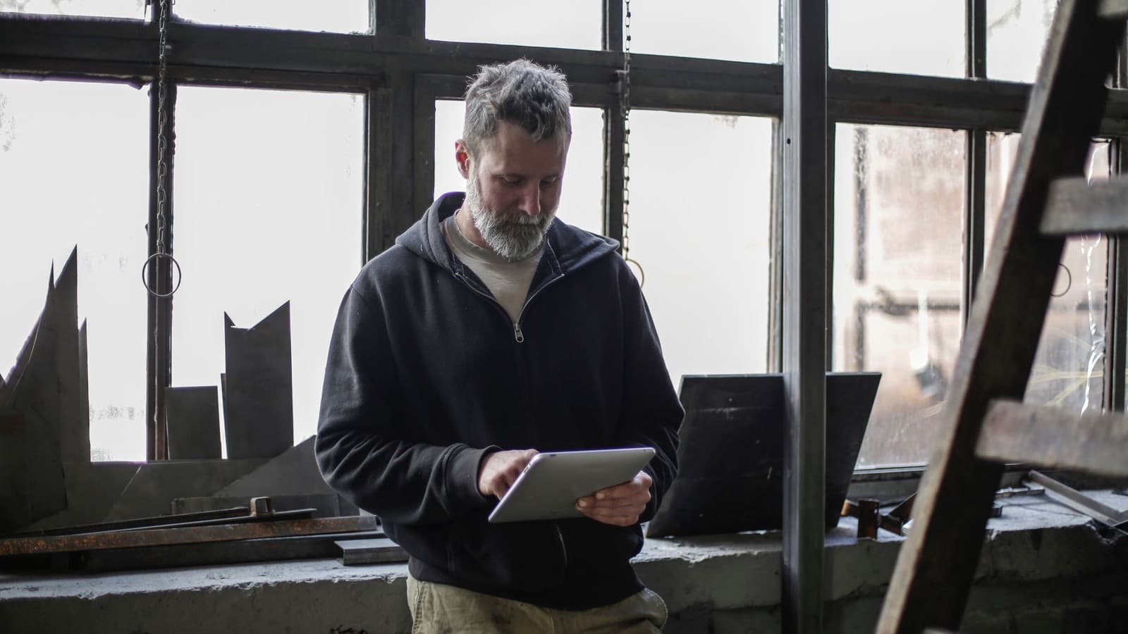Vakman bekijkt een tablet in een werkplaats met gereedschap en metaalonderdelen