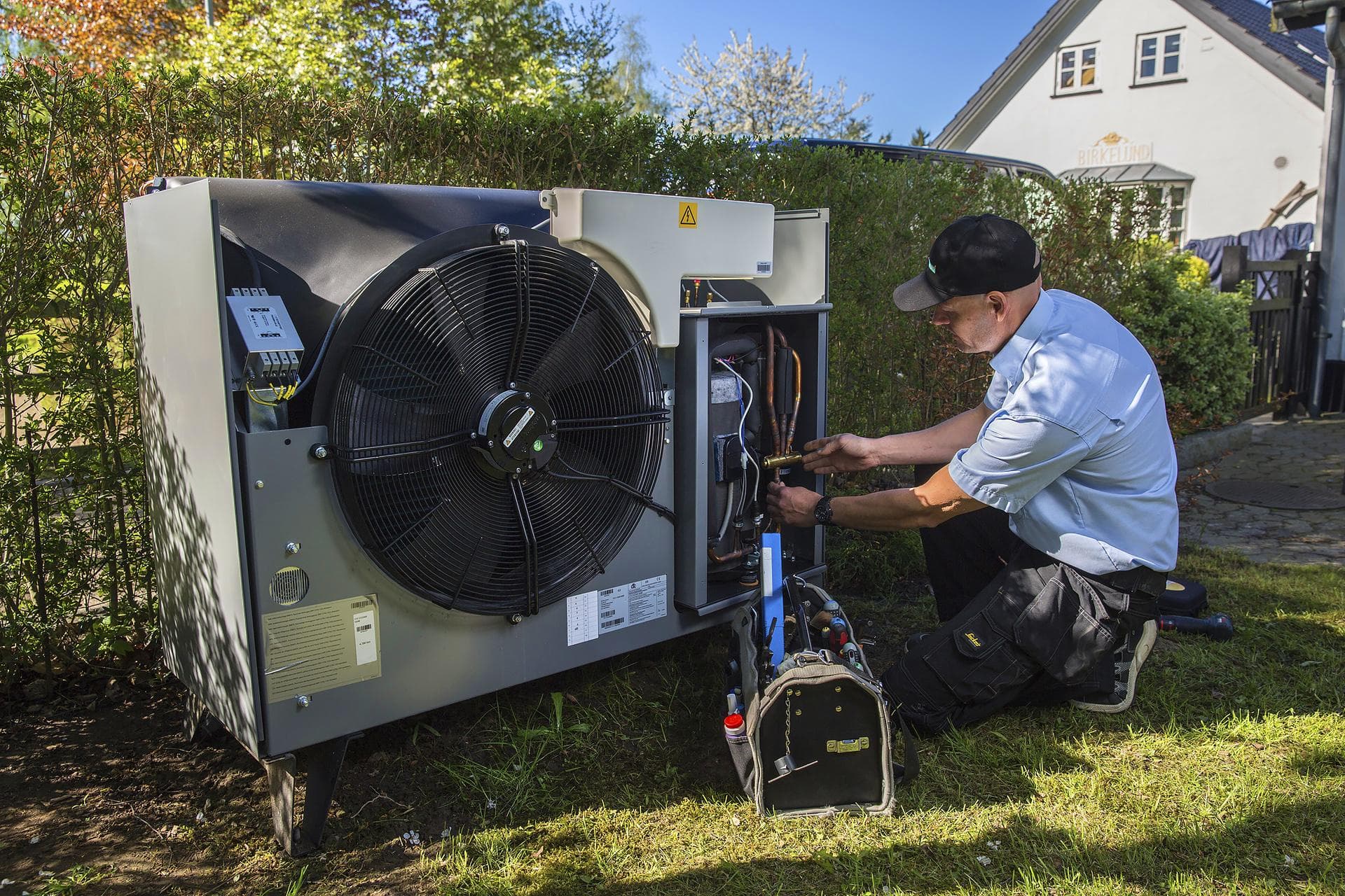 Monteur werkt aan de buitenunit van een warmtepomp naast een woning